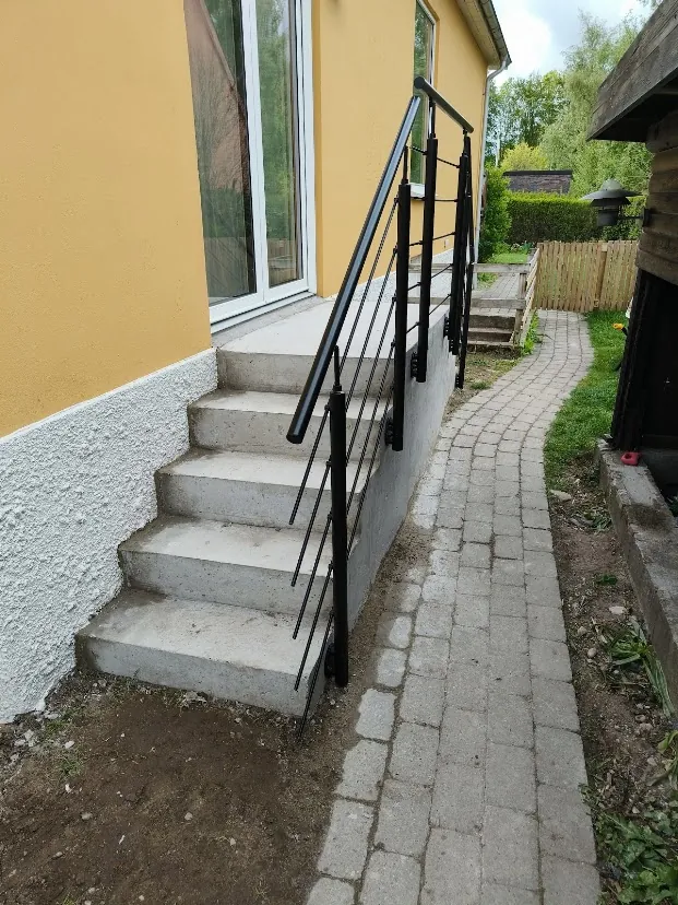Betontrappe med sort gelænder ved gul husfacade